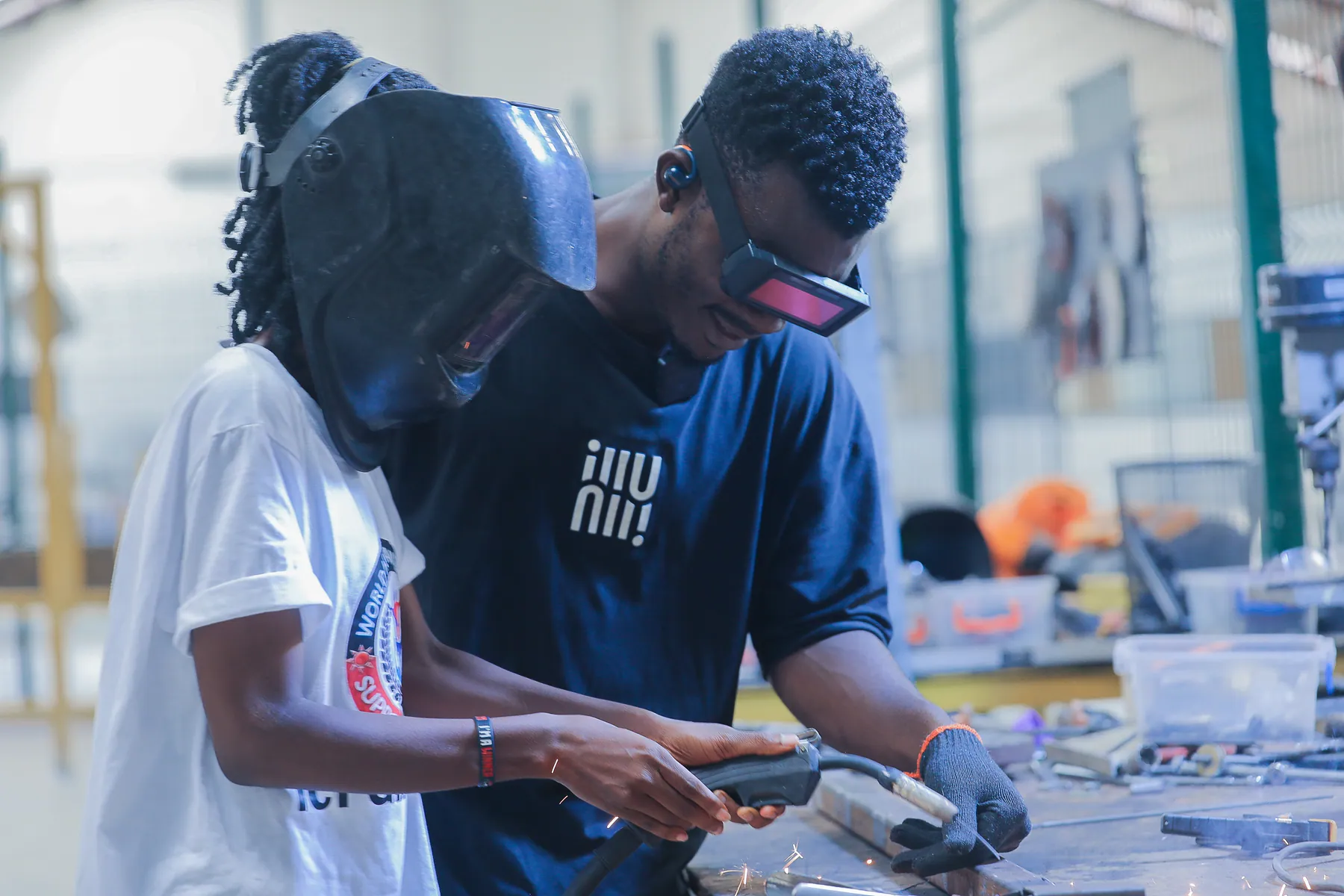 Instructor guiding a Girls in ICT Club participant through welding equipment